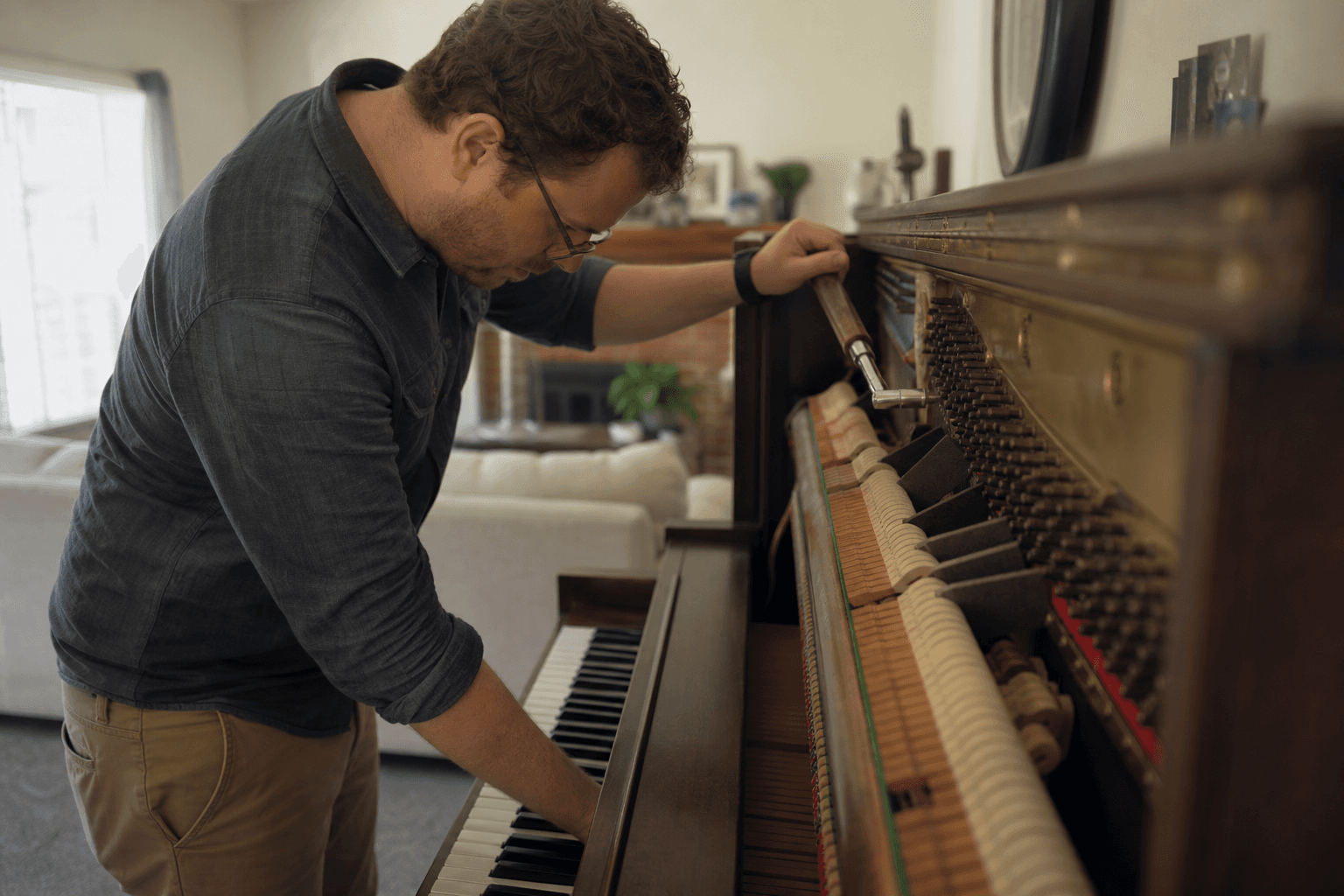 Piano tuner adjusting the pins inside an open upright piano in a living room